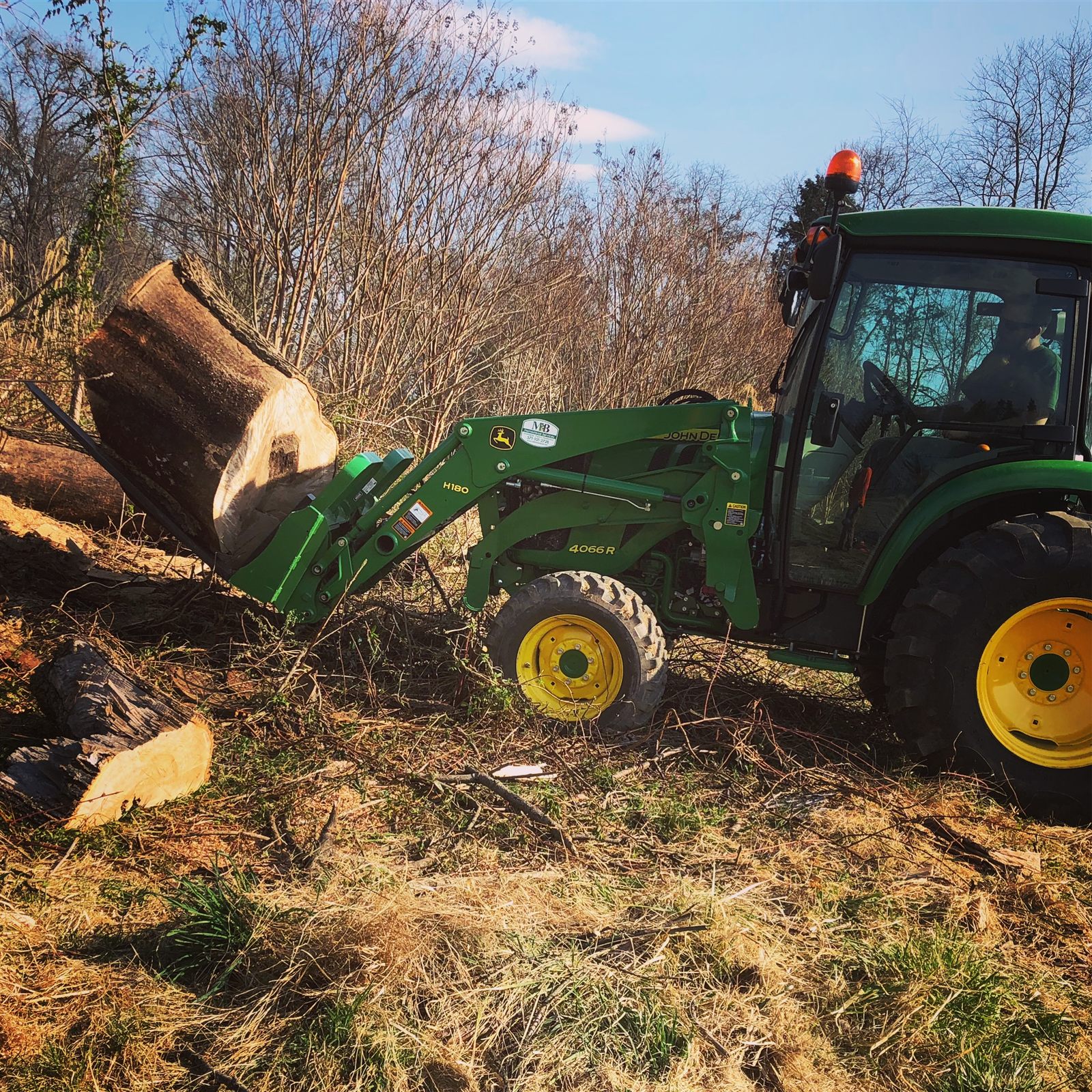 MB Homestead John Deere tractor lifting a large hardwood log during land clearing